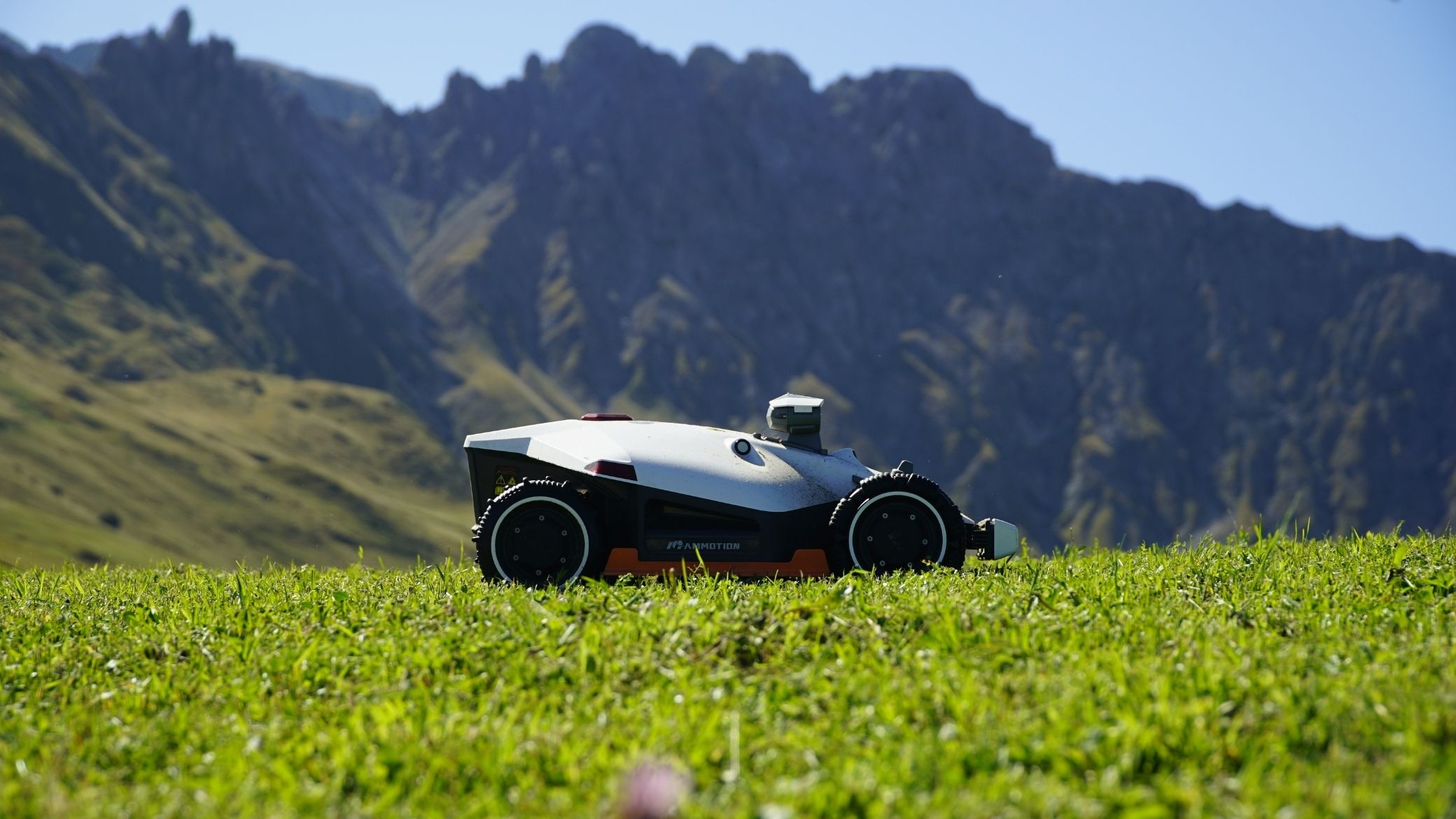 Mammotion AWD robot mower on a mountain meadow with steep relief in the background